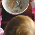 Seen from above, a young child eats a bowl of cereal