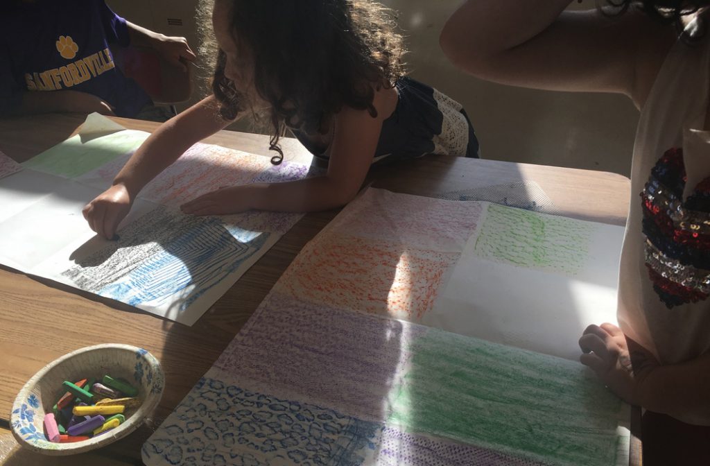 An elementary girl draws on paper with chalk