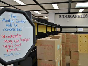 View of emply shelving, piles of cardboard boxes marked as "biography section," and sign annoucing the Media Center rennovation.