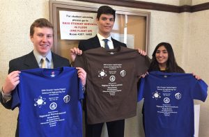 Three students holding event t-shirts.