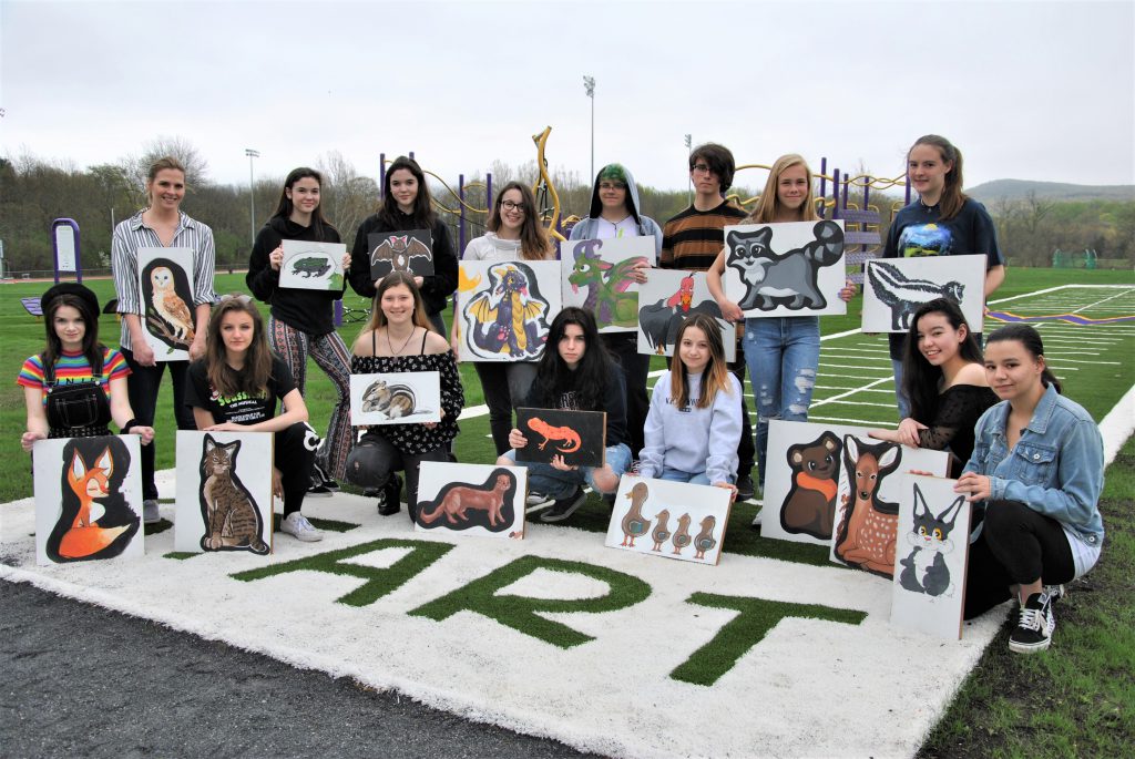 Group photo of students holding their paintings of animals outside.
