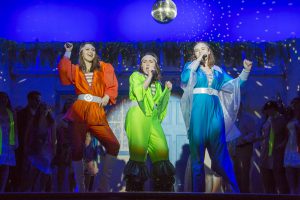 Three singers dressed in 70s pop stage costumes