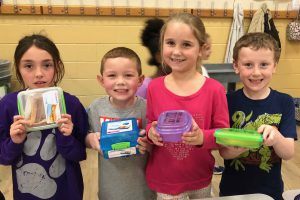 Four students hold reusable lunch containers.