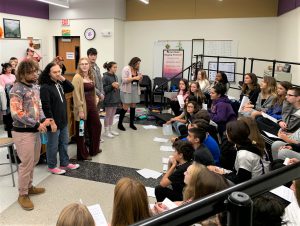 A group of high school students presents to a class of younger students in a music room