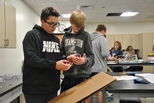 Two students focus on a lab - one student pushes a car down a cardboard ramp while the other holds a stopwatch